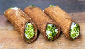Cannoli filled with ricotta and dipped in pistachios placed on a wooden chopping board