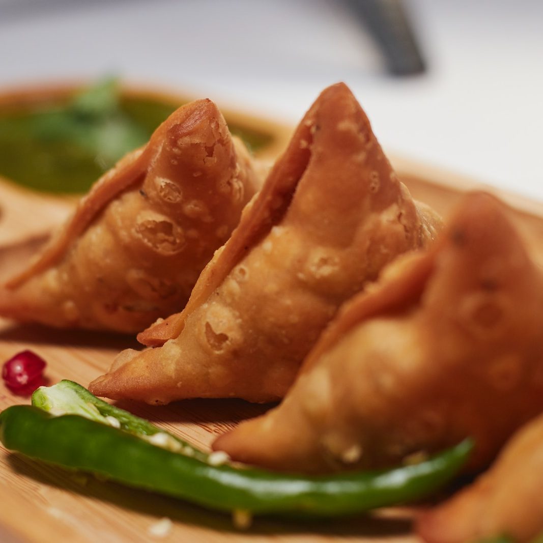 3 samosas on a wooden chopping board with edible decoration