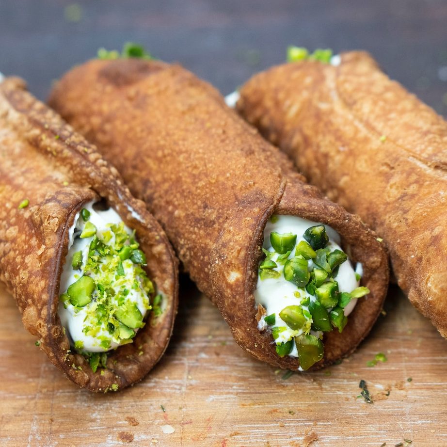 Cannoli filled with ricotta and dipped in pistachios placed on a wooden chopping board